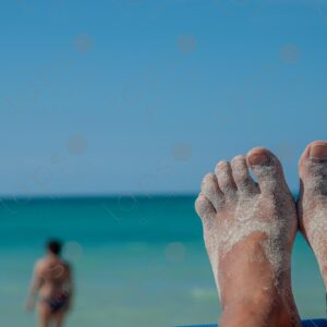 Brown feet in sand, turquoise sea in the background