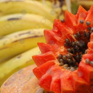 Half cut papaya with orange flesh and seeds with bananas in the background