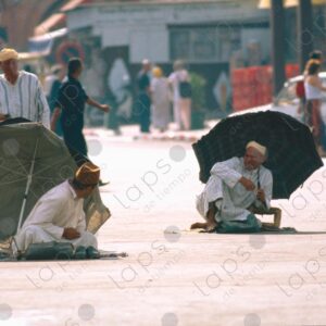 Two Men in Traditional Attire Sitting with Umbrella at Jemaa el-Fna Square, Marrakech