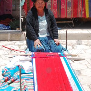 Indigenous woman on the ground shows her red loom