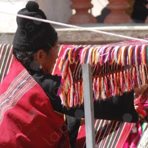 Indigenous woman working on a red loom with lines 1