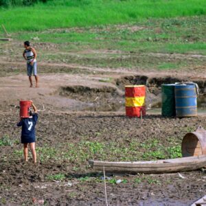 Person carrying a bucket in the mud on the riverbank