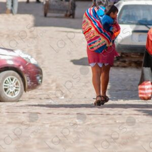 Woman walks carrying a child on her back in an aguayo 3