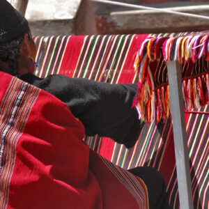 Indigenous woman working on a red loom with lines 2