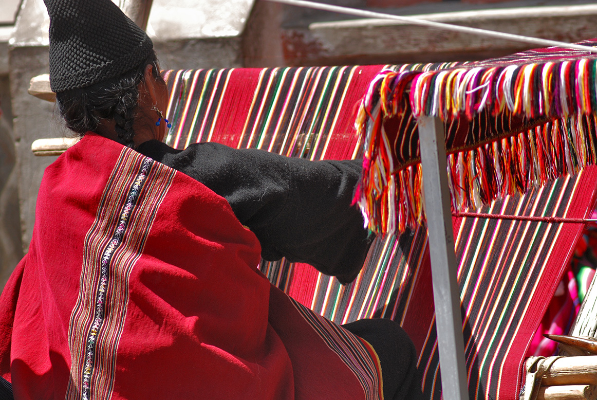 Indigenous woman working on a red loom with lines 2